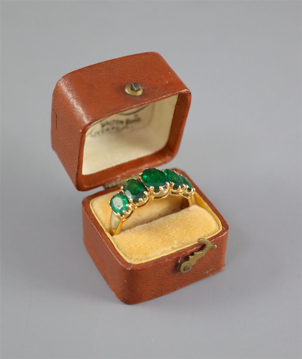 A mid to late 20th century gold and graduated five stone oval cut emerald set half hoop ring,